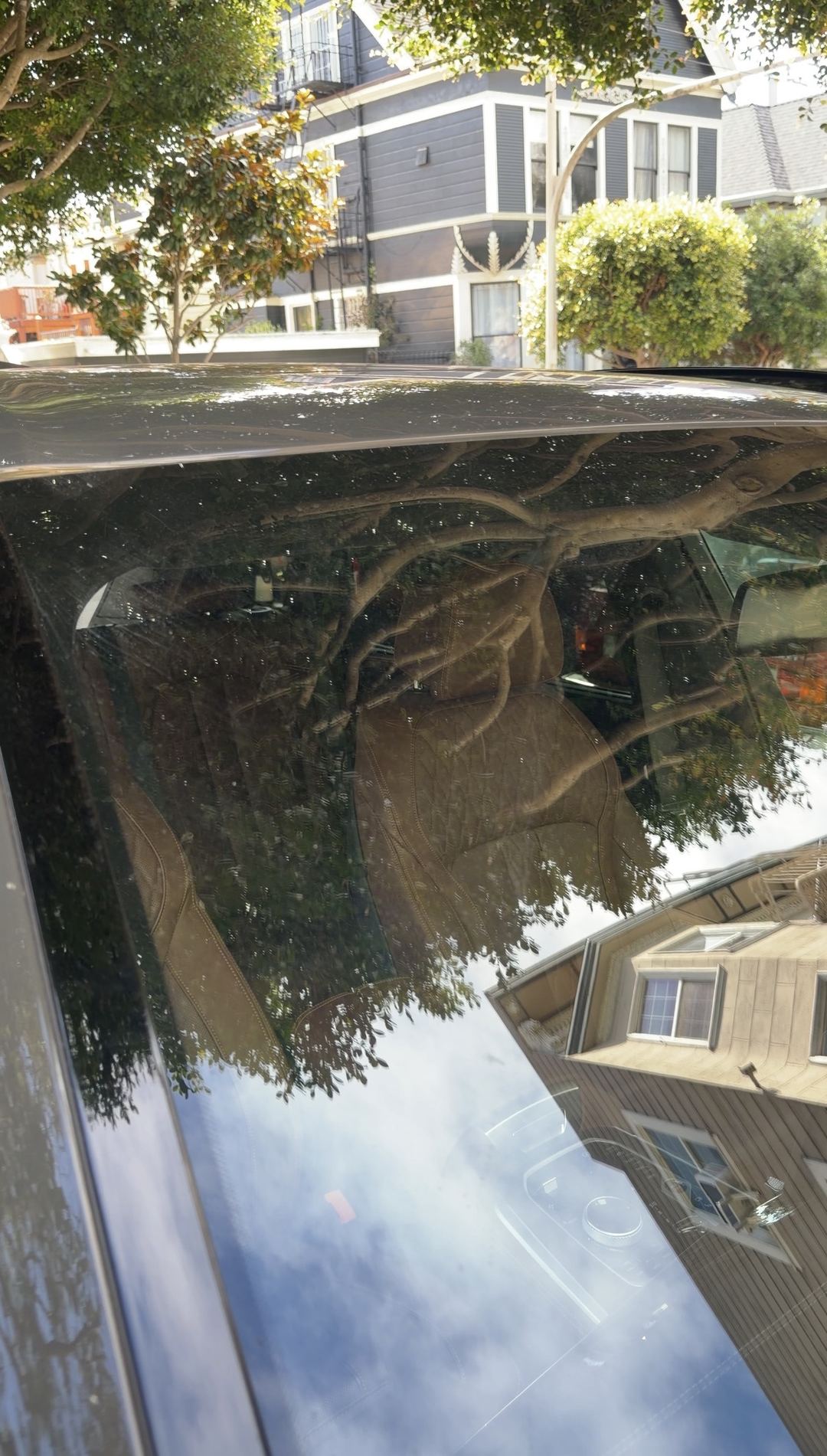 Roof and rear quarter glass of a dark grey BMW X5 before washing, speckled with dried water spots