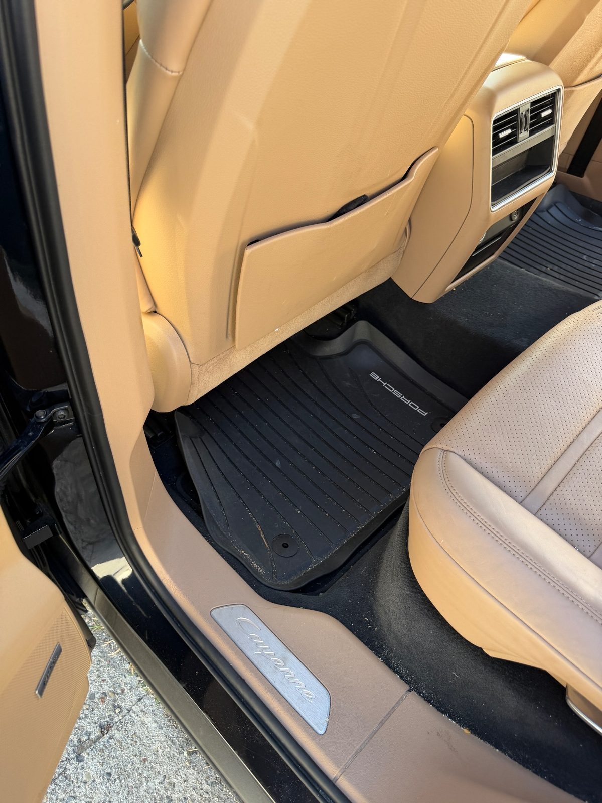 Rear footwell of a dark blue Porsche Cayenne before cleaning, rubber mat covered in crumbs and lint