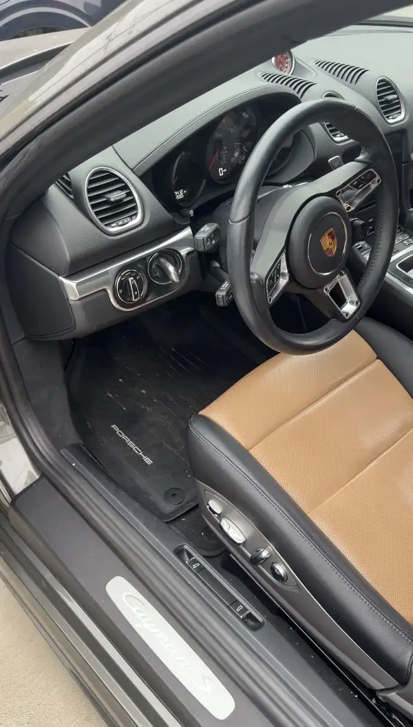 Driver's footwell and Cayman S door sill of a Porsche 718 with debris on the floor mat before an interior detail.