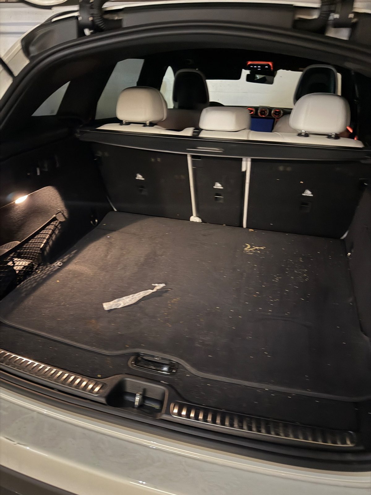 Cargo area of a white Mercedes GLC before detailing, black mat covered in crumbs, debris and a crumpled wrapper