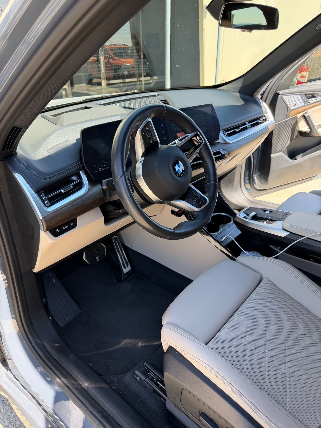 Driver footwell of a grey BMW X1 before detailing, with dust and lint on the carpet