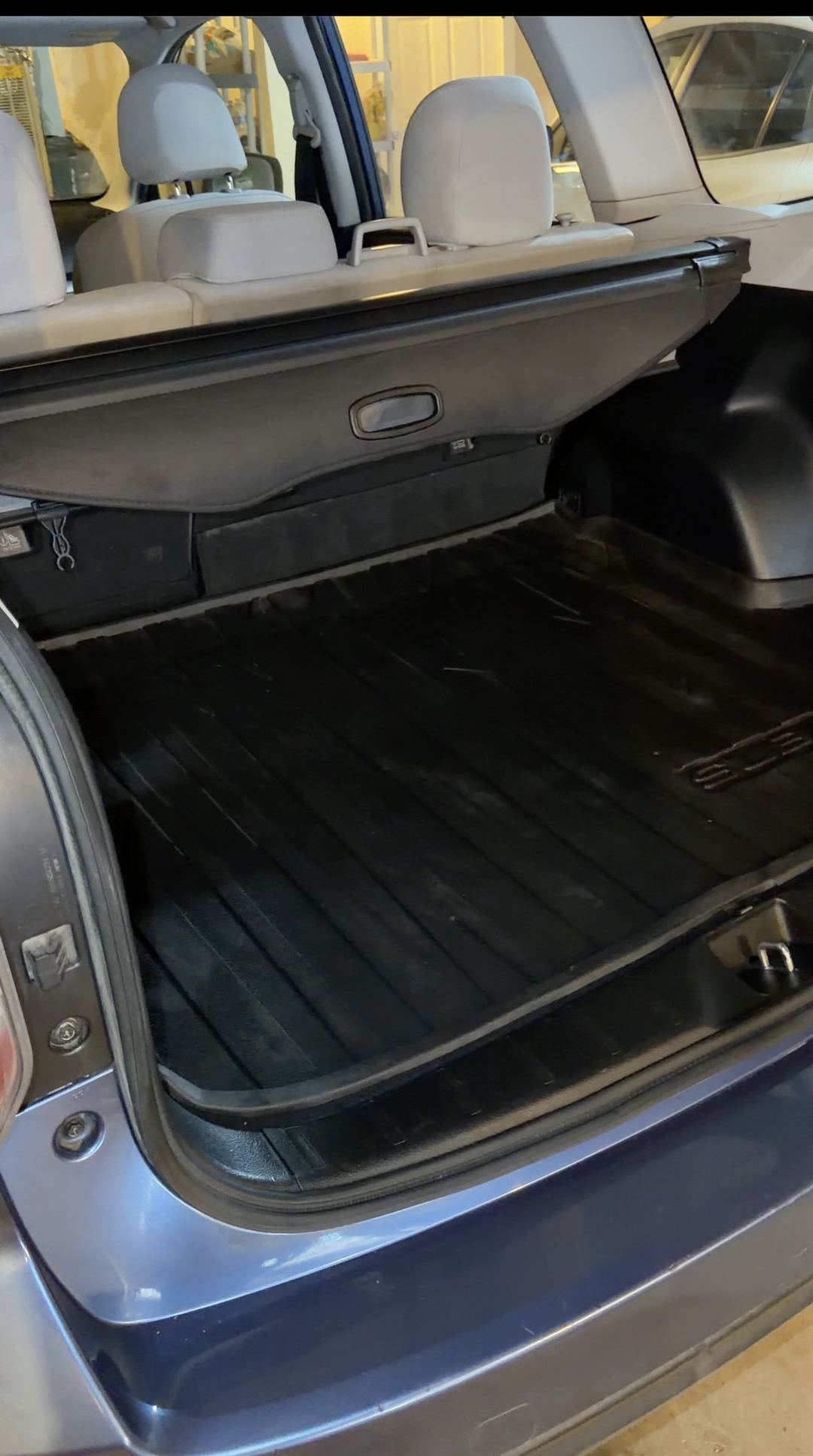 Open cargo area of a blue Subaru Forester with the rubber cargo tray empty and the retractable cargo cover in place.