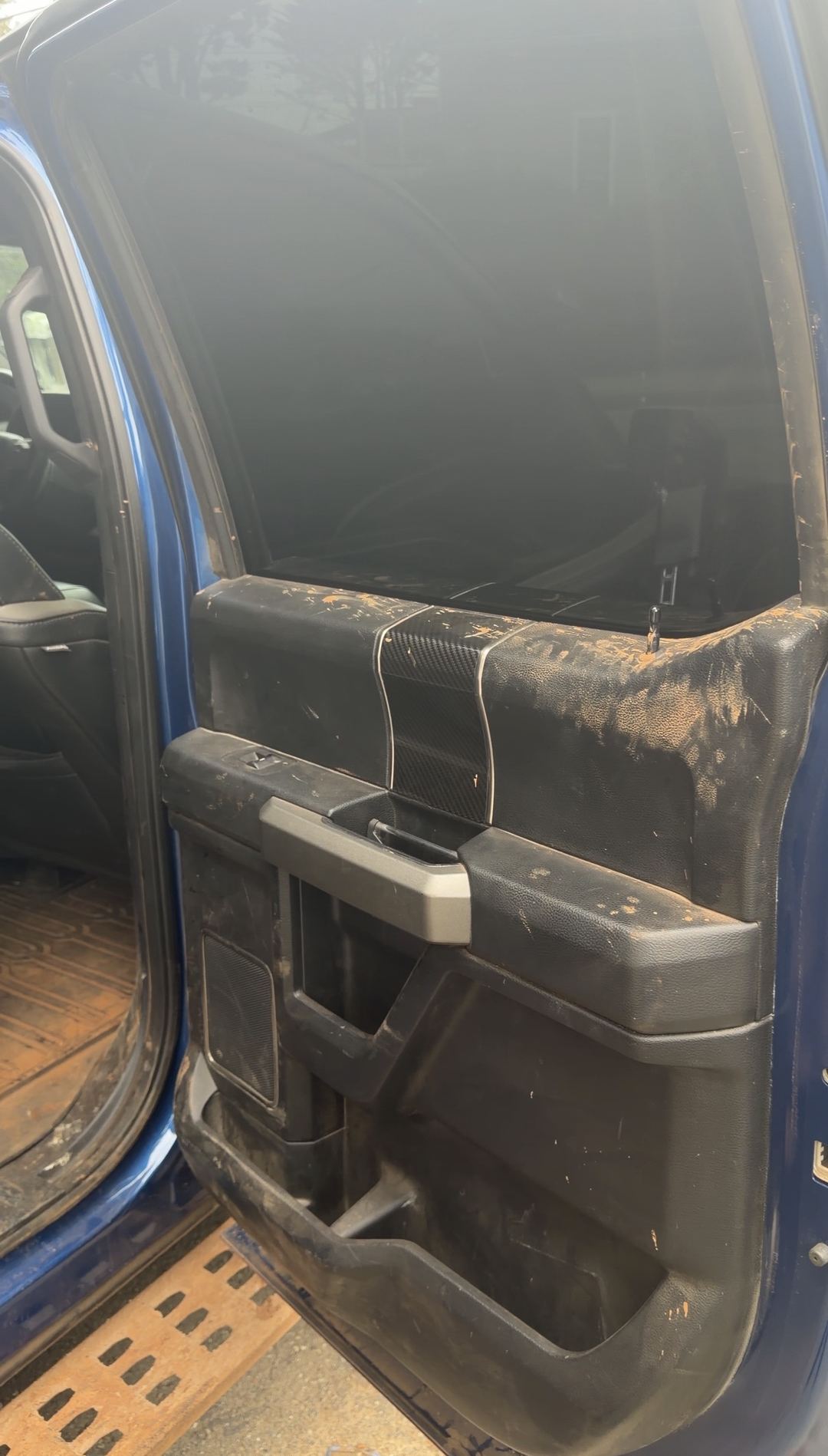 Rear door panel of a Ford F-150 Raptor with dried mud splattered across the armrest