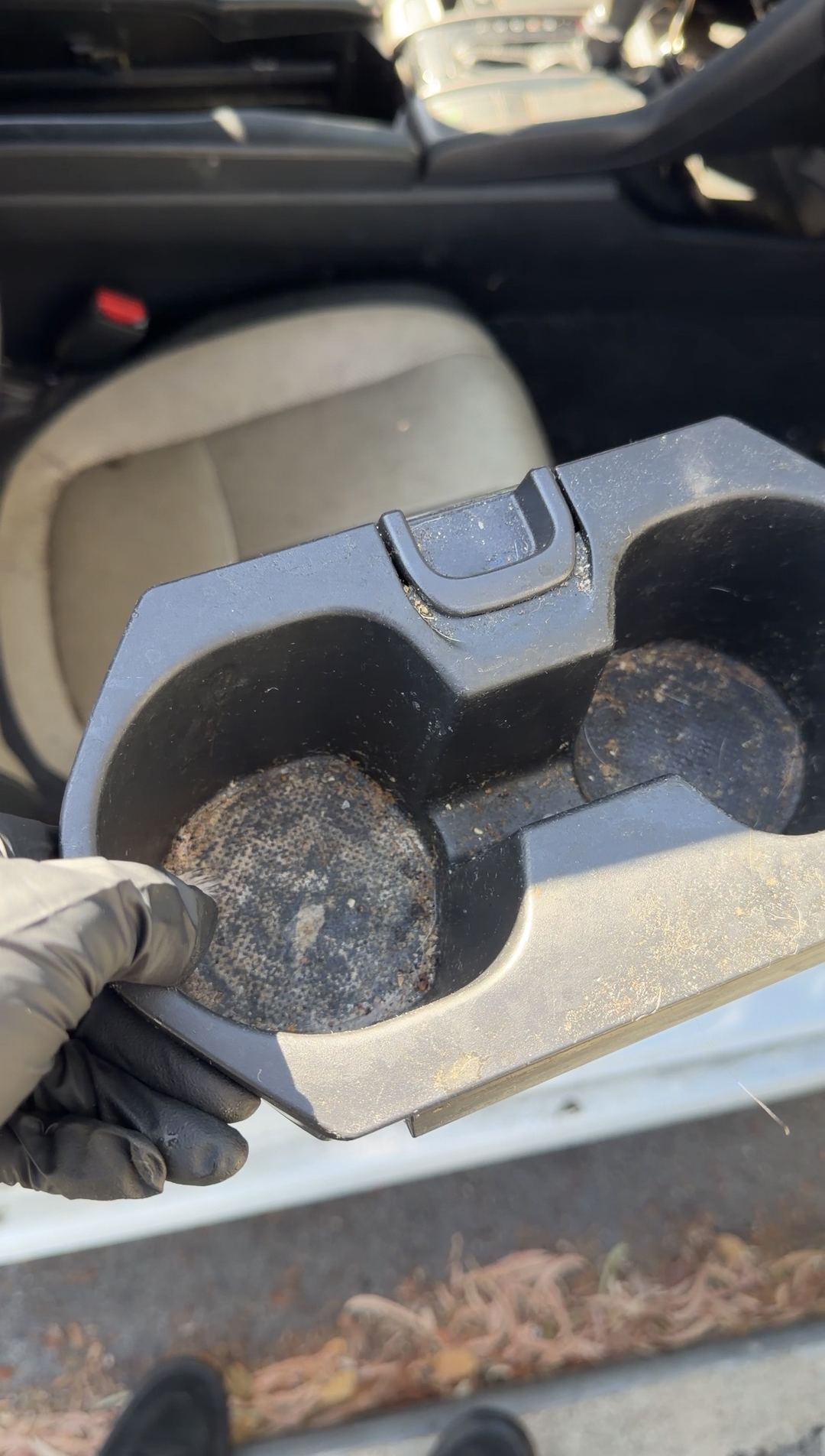 Gloved hand holding a Honda Civic cupholder insert removed from the console, both wells caked with dried residue