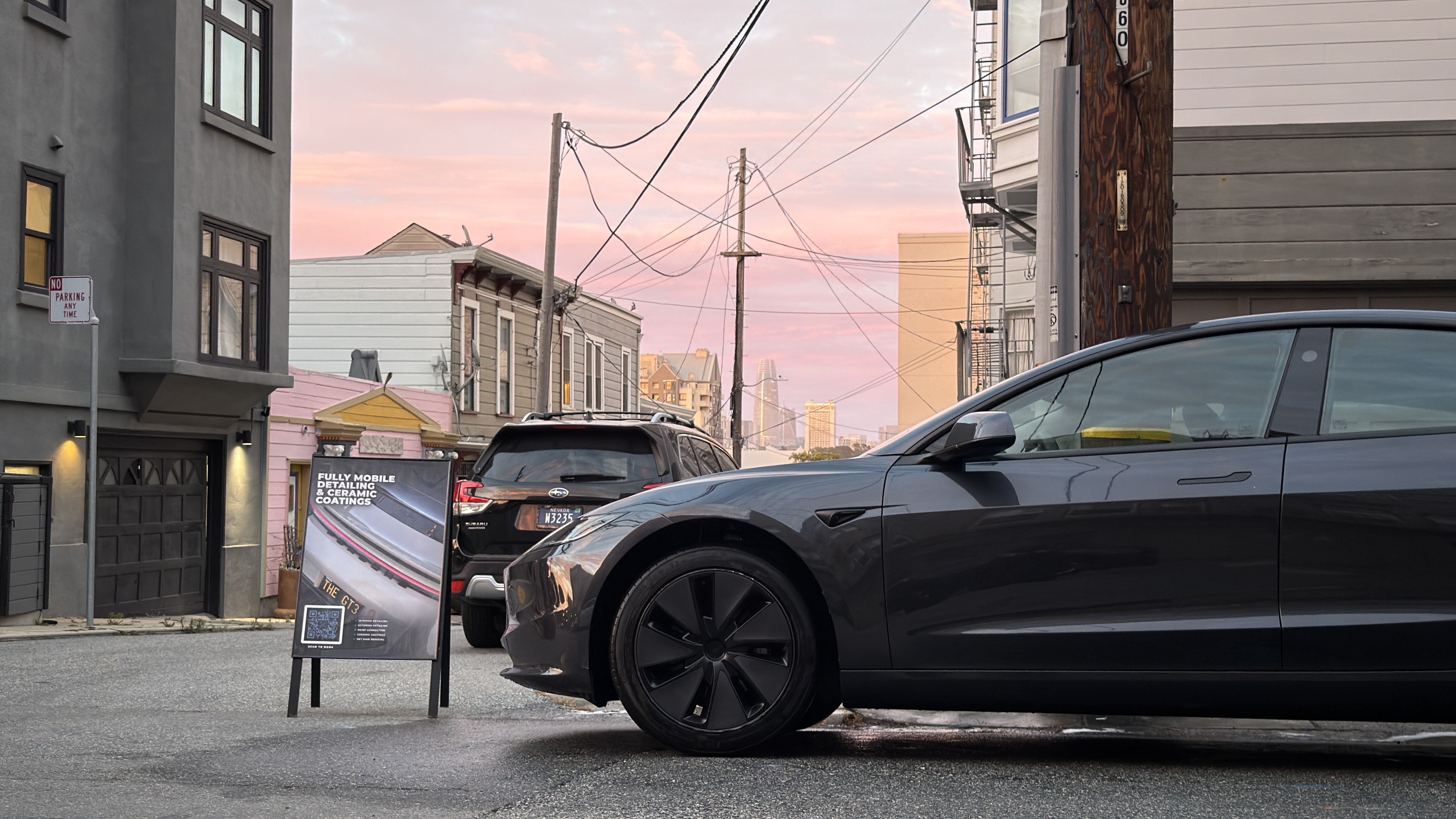 SF City Wash detailed Tesla Model 3 parked on a San Francisco street at dusk with the city skyline behind it