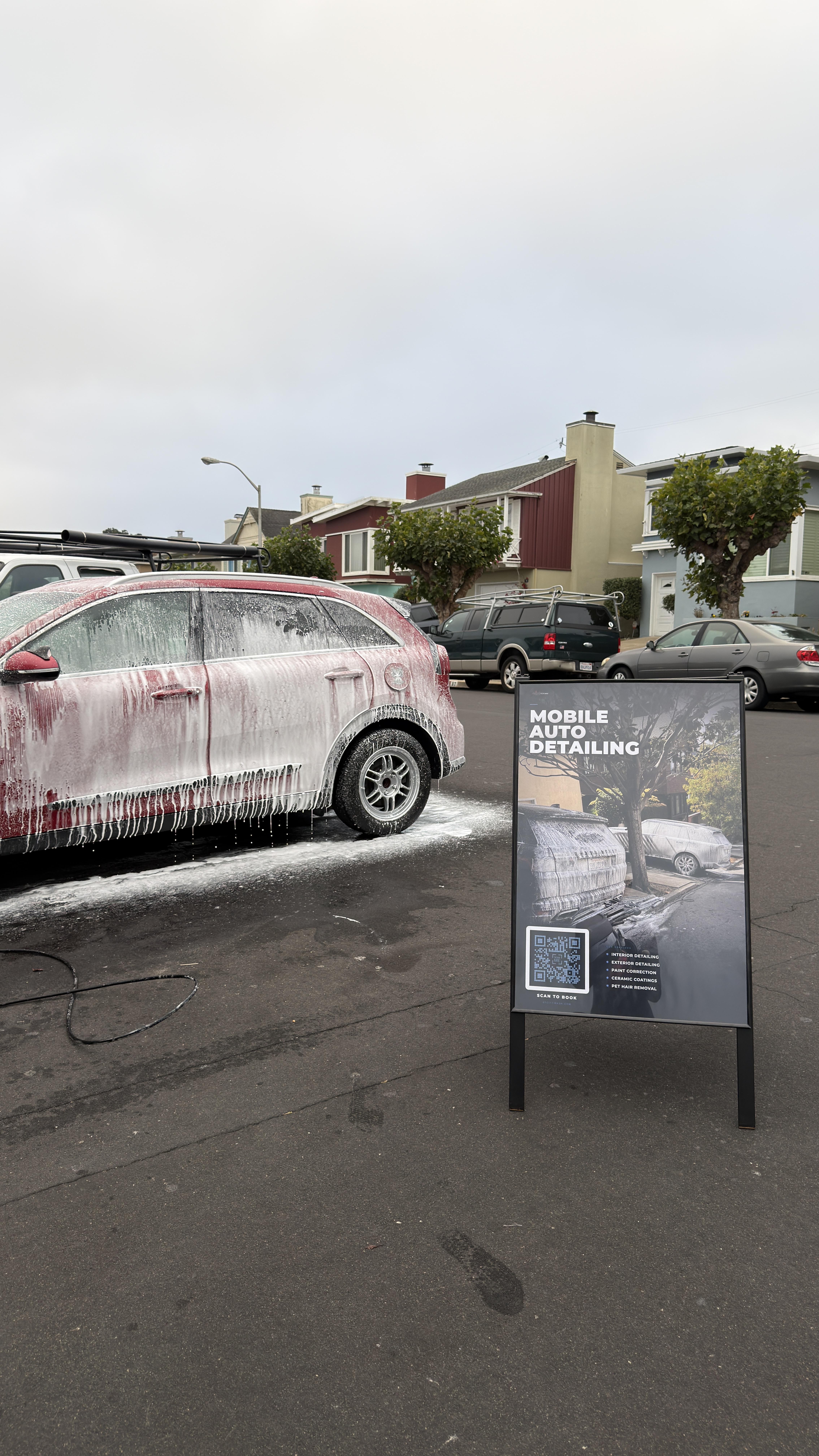 SF City Wash mobile detailing setup foam pre-washing a red 2019 Kia Niro on a residential street in Westlake, with branded A-frame sign in the foreground