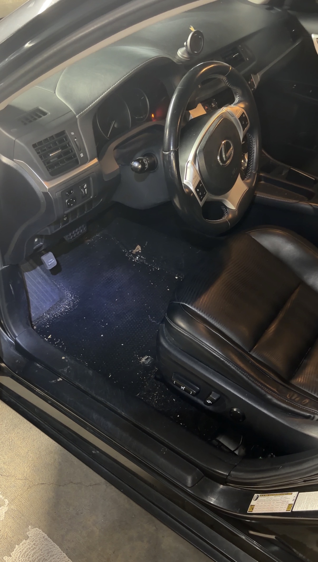 Driver footwell before detail, mat pulled back with debris on carpet