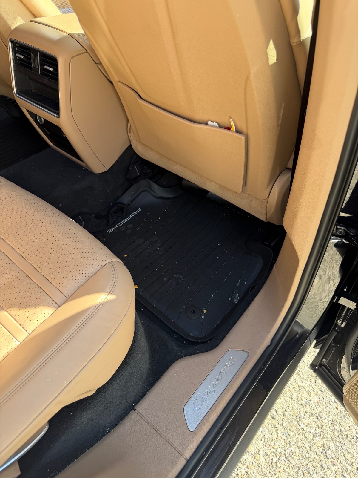 Rear footwell of a dark blue Porsche Cayenne before cleaning, crumbs and a spill on the rubber mat
