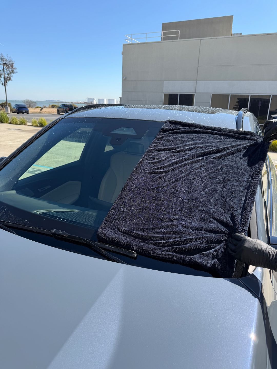 Drying the windshield of a grey BMW X1 with a microfibre towel