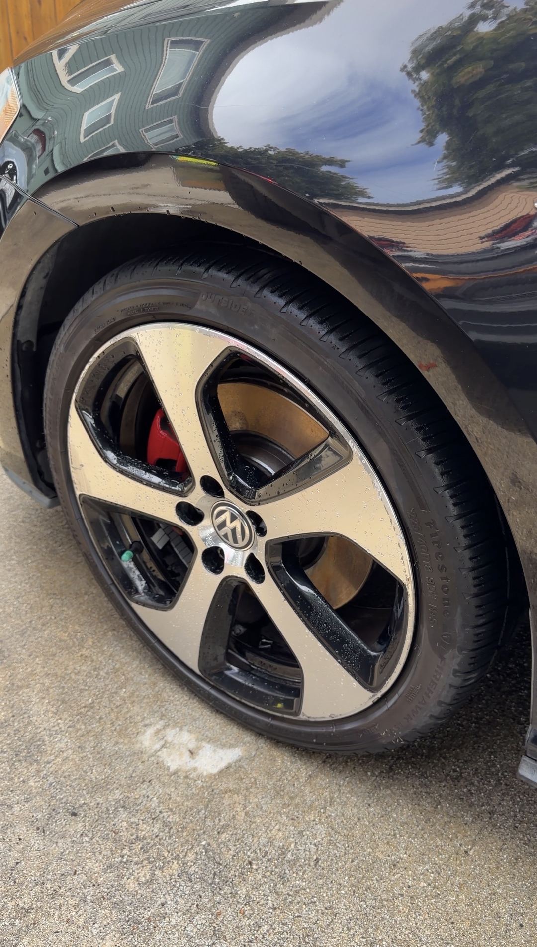 Front-left wheel of a black VW GTI after cleaning, wet tyre and red brake caliper