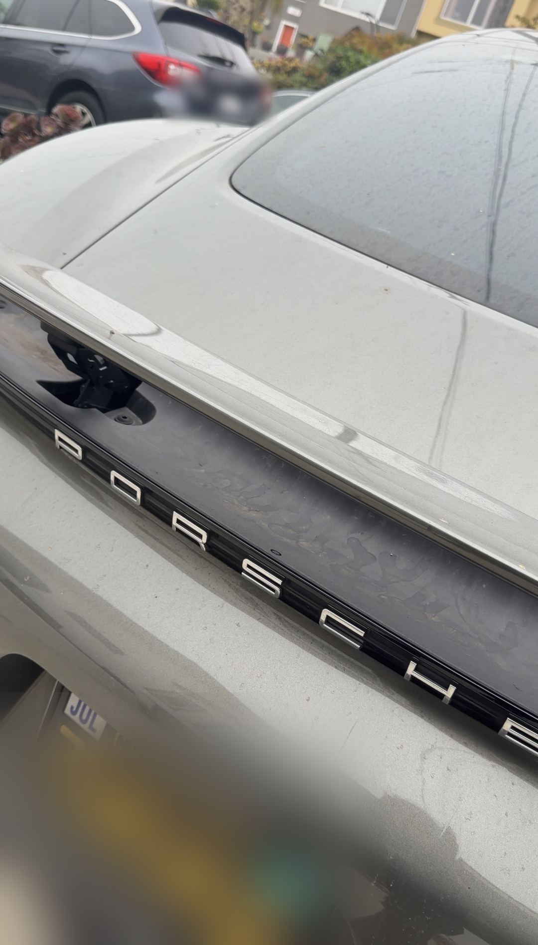 Dust-dulled gloss black rear badge band of a Porsche 718 Cayman S before detailing.