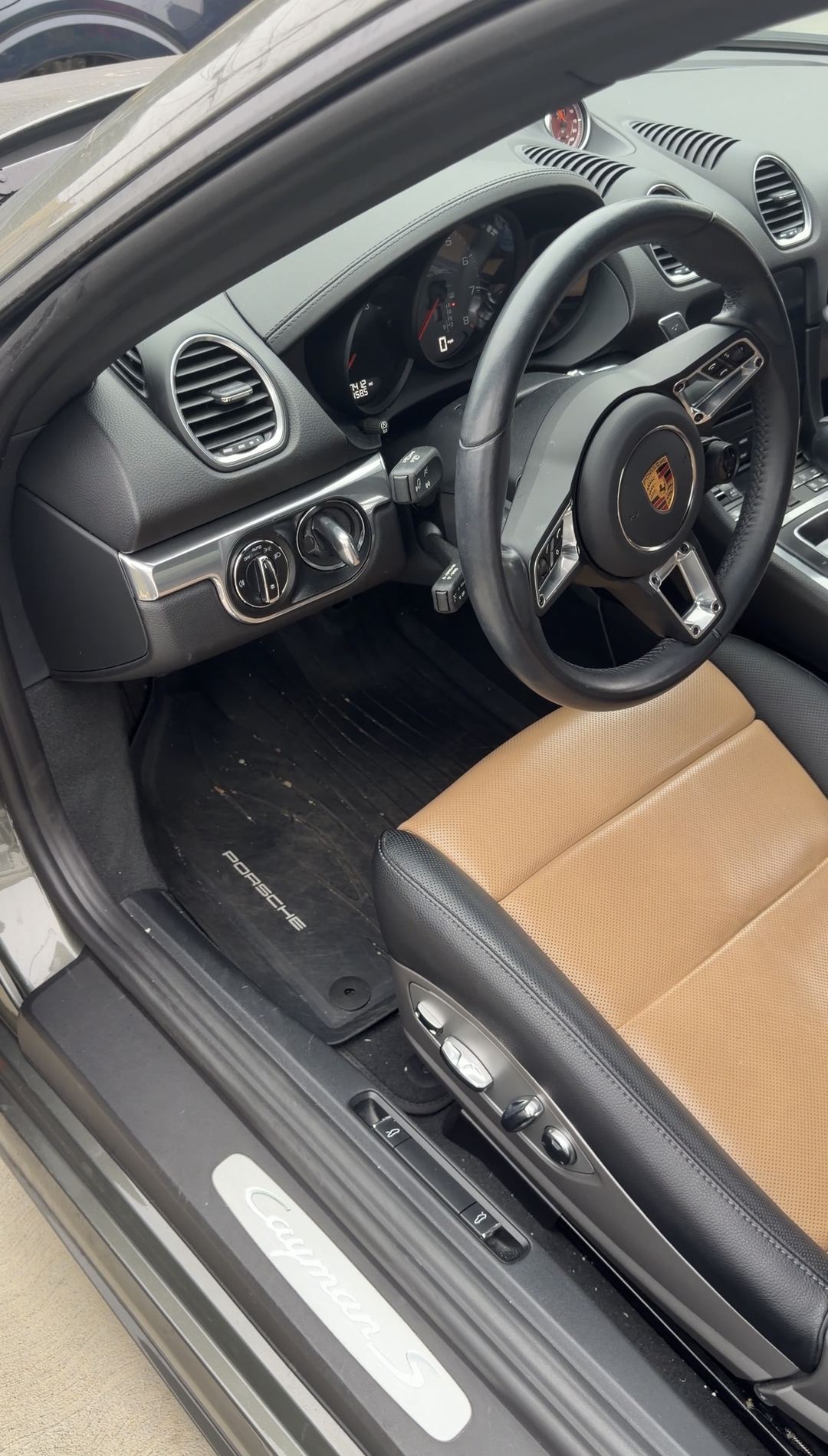 Driver's footwell and Cayman S door sill of a Porsche 718 with debris on the floor mat before an interior detail.