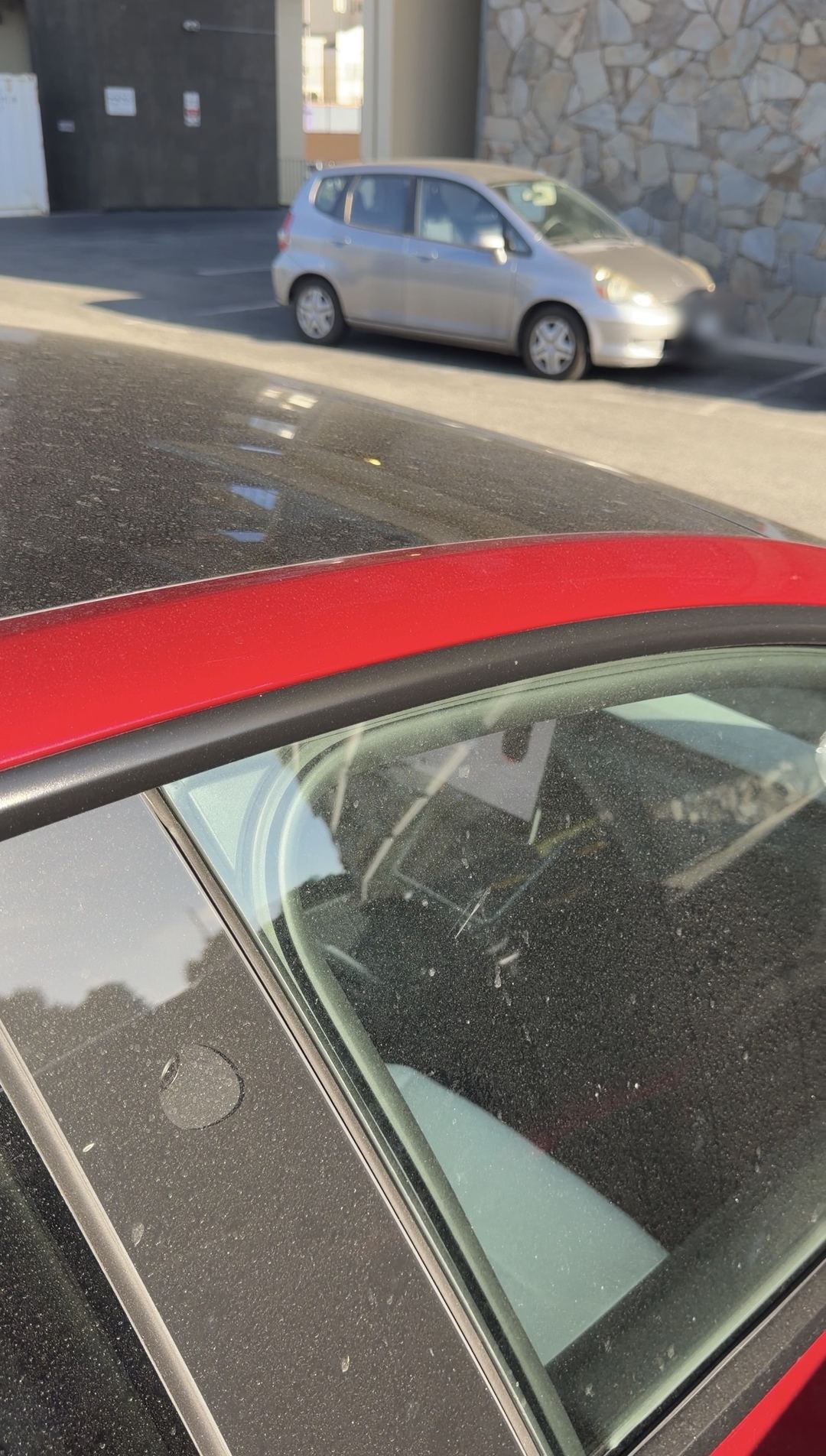 Thick dust coating the glass roof of a red Tesla Model Y in a parking lot
