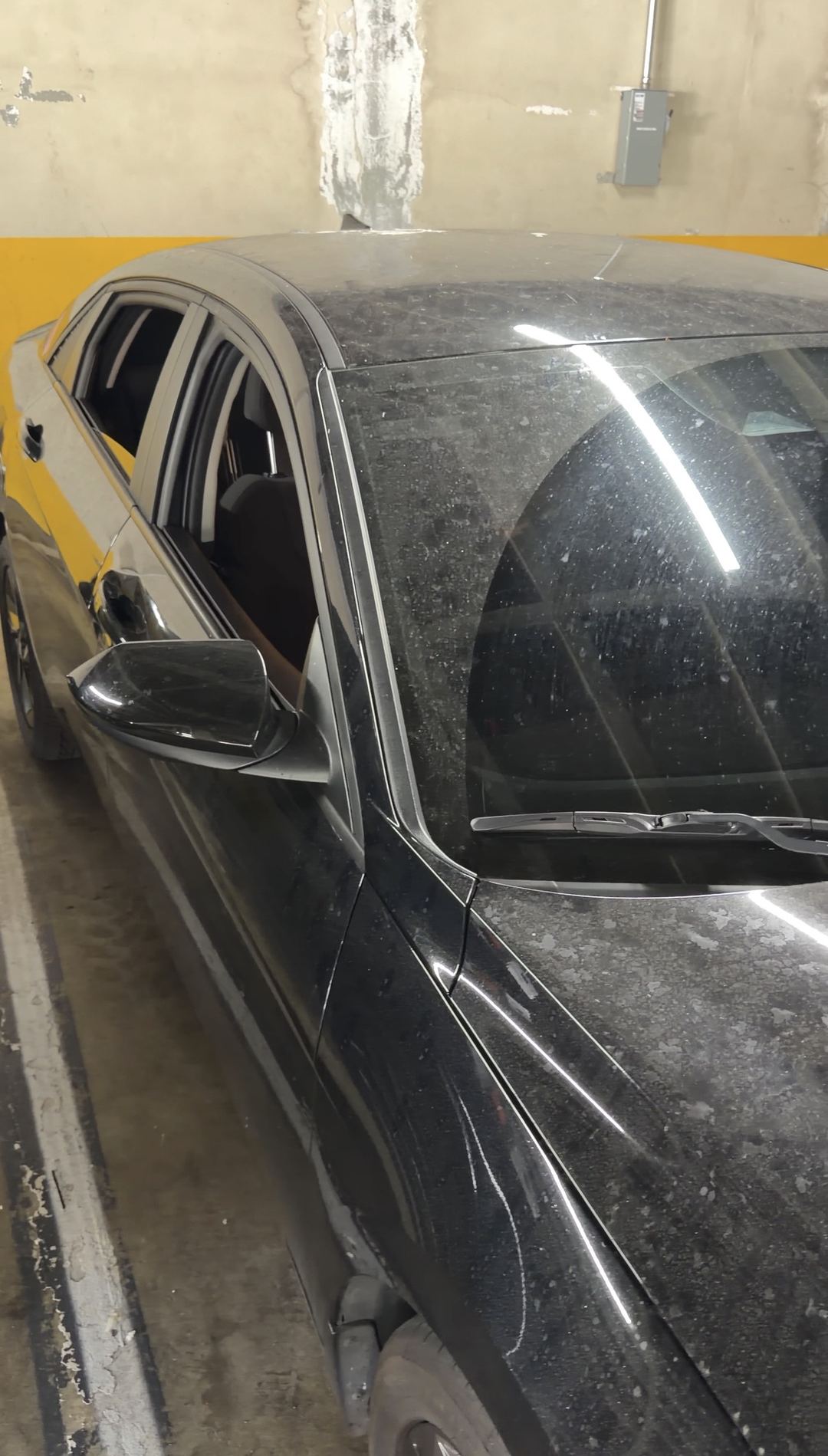 Driver side of a dusty black Hyundai Elantra with the windows down in a parking garage