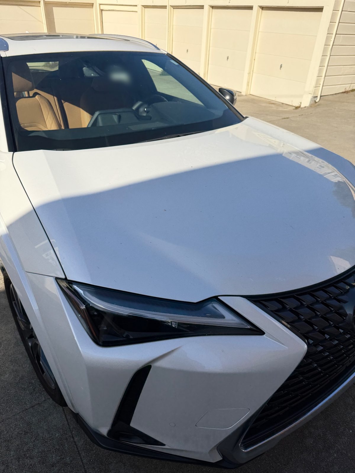 Front three-quarter of a white Lexus UX before washing, with a dusty hood