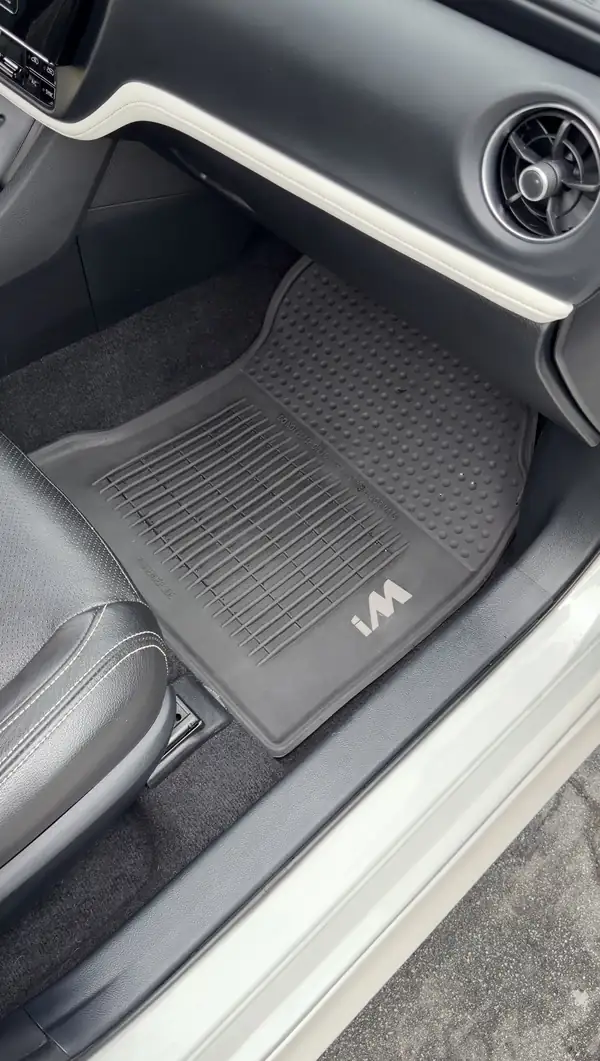 Front passenger footwell of a Toyota Corolla iM after cleaning, showing a spotless iM-branded rubber floor liner and clean carpet and sill.
