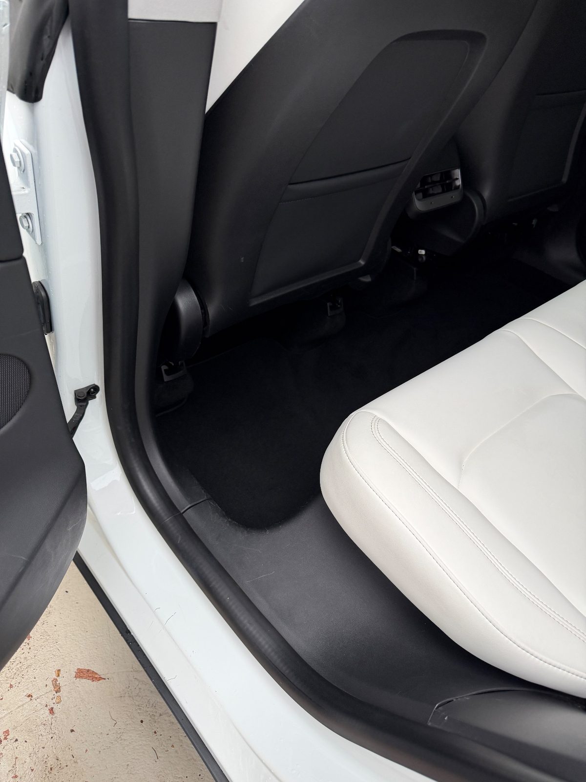 Rear footwell of a white Tesla Model Y after detailing, with a clean vacuumed carpet mat
