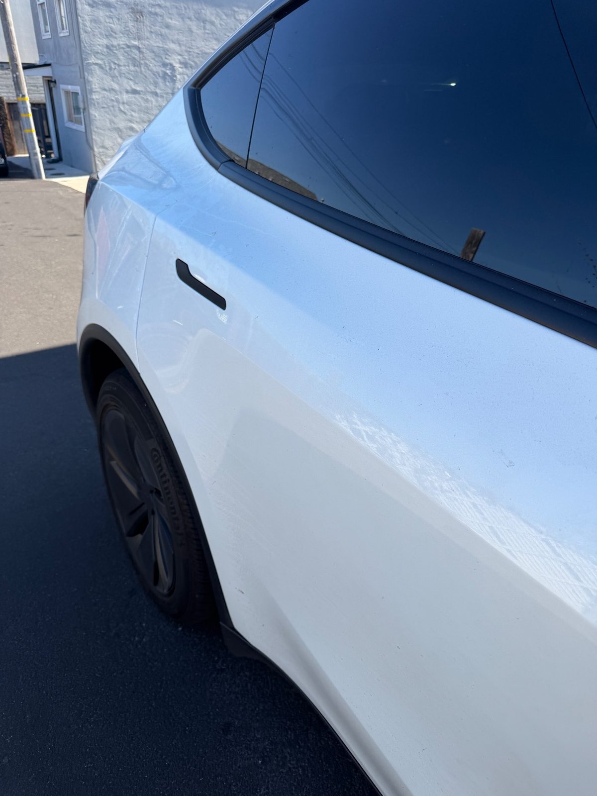 Rear door and quarter of a white Tesla Model Y before washing, dusty finish with water spots
