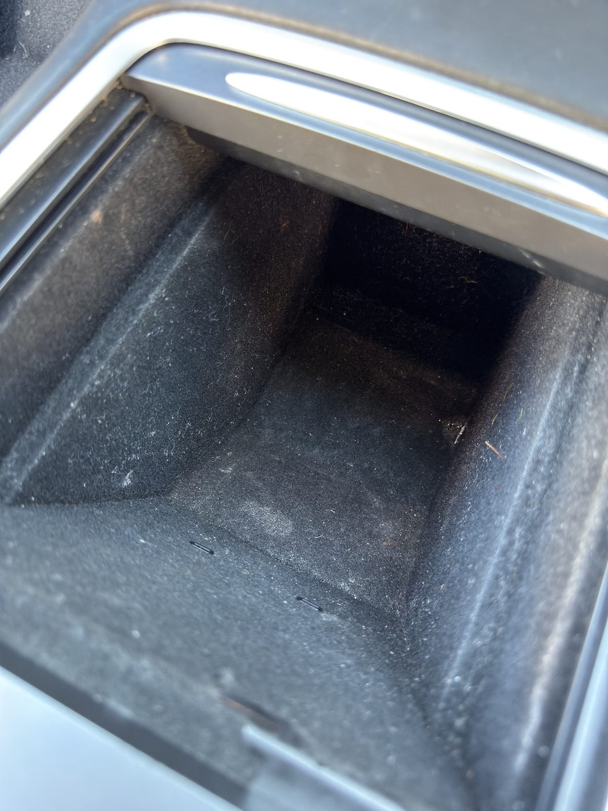 Dusty console storage tray in a white Tesla Model Y before cleaning