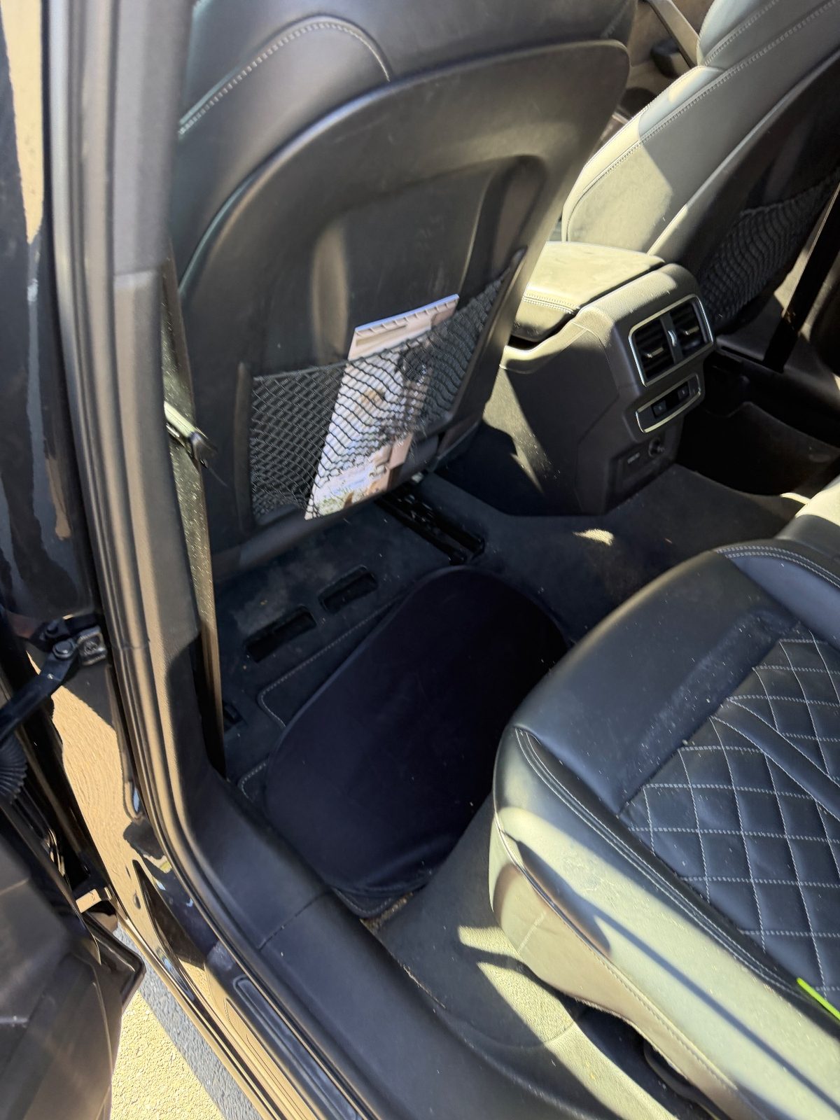 Rear footwell of an Audi SQ5 before detailing, with dust and grit on the carpet and a cushion left on the floor