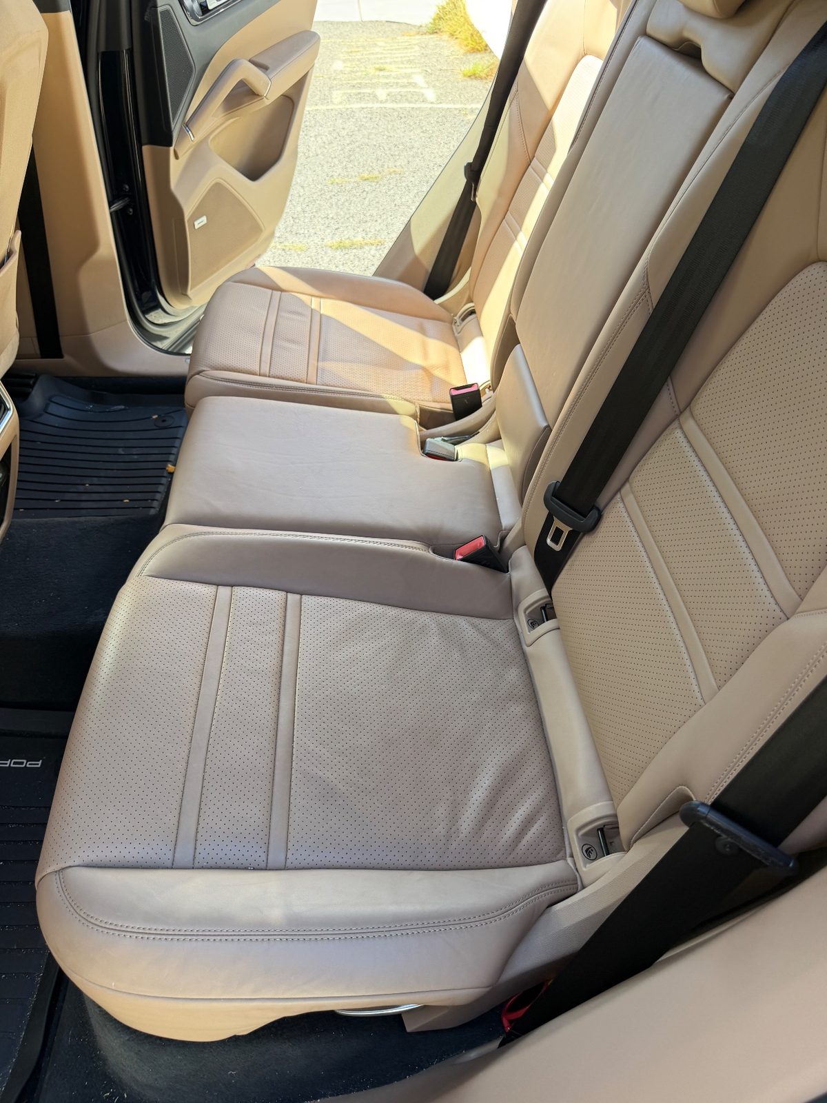 Rear seat of a dark blue Porsche Cayenne before cleaning, tan leather cushion dull and dusty