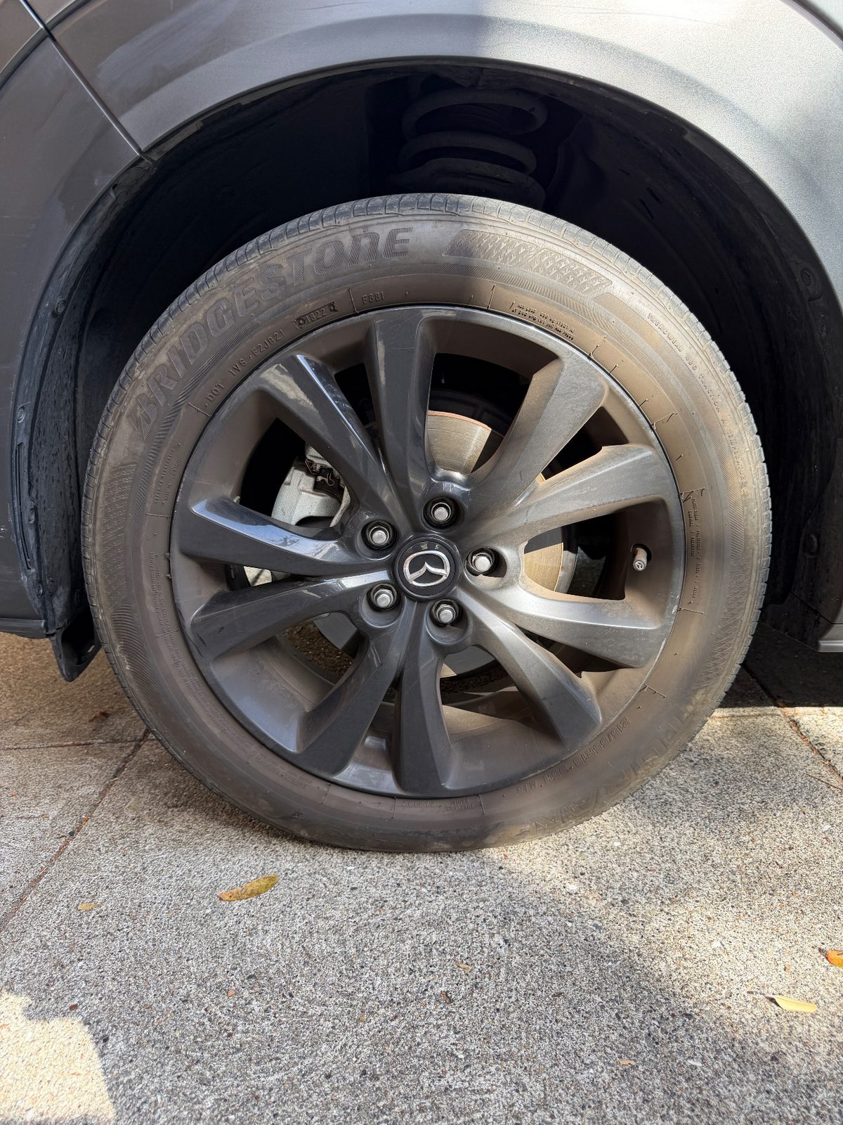 Front wheel of a grey Mazda CX-30 before cleaning, brake dust on the alloy