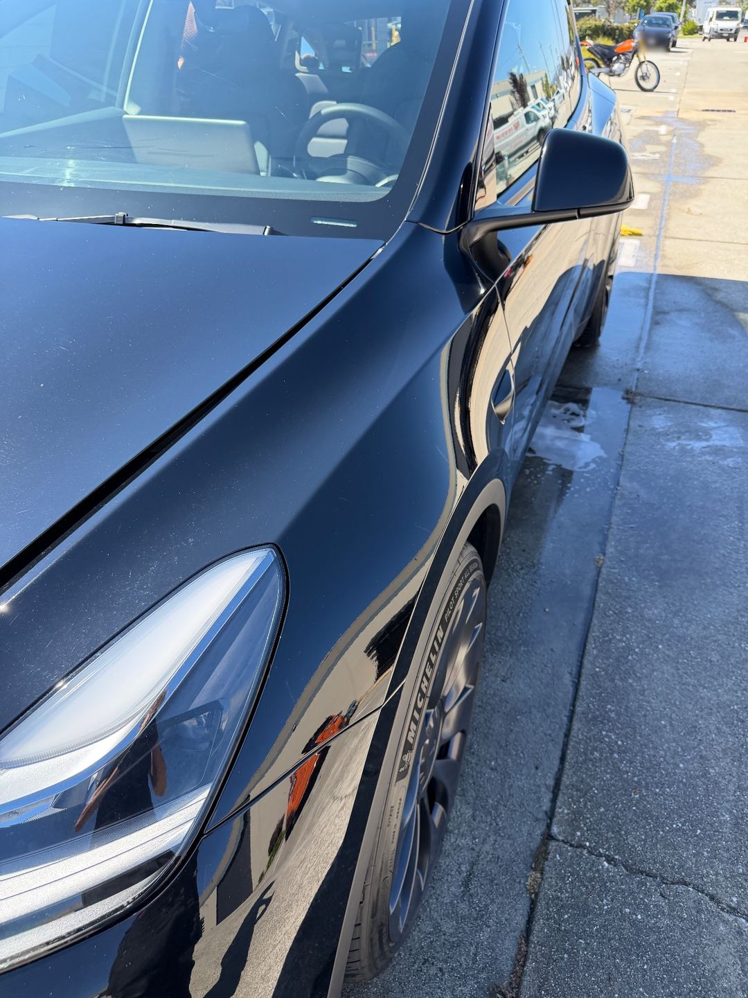 Glossy left front fender and headlight of a black Tesla Model Y after its wash