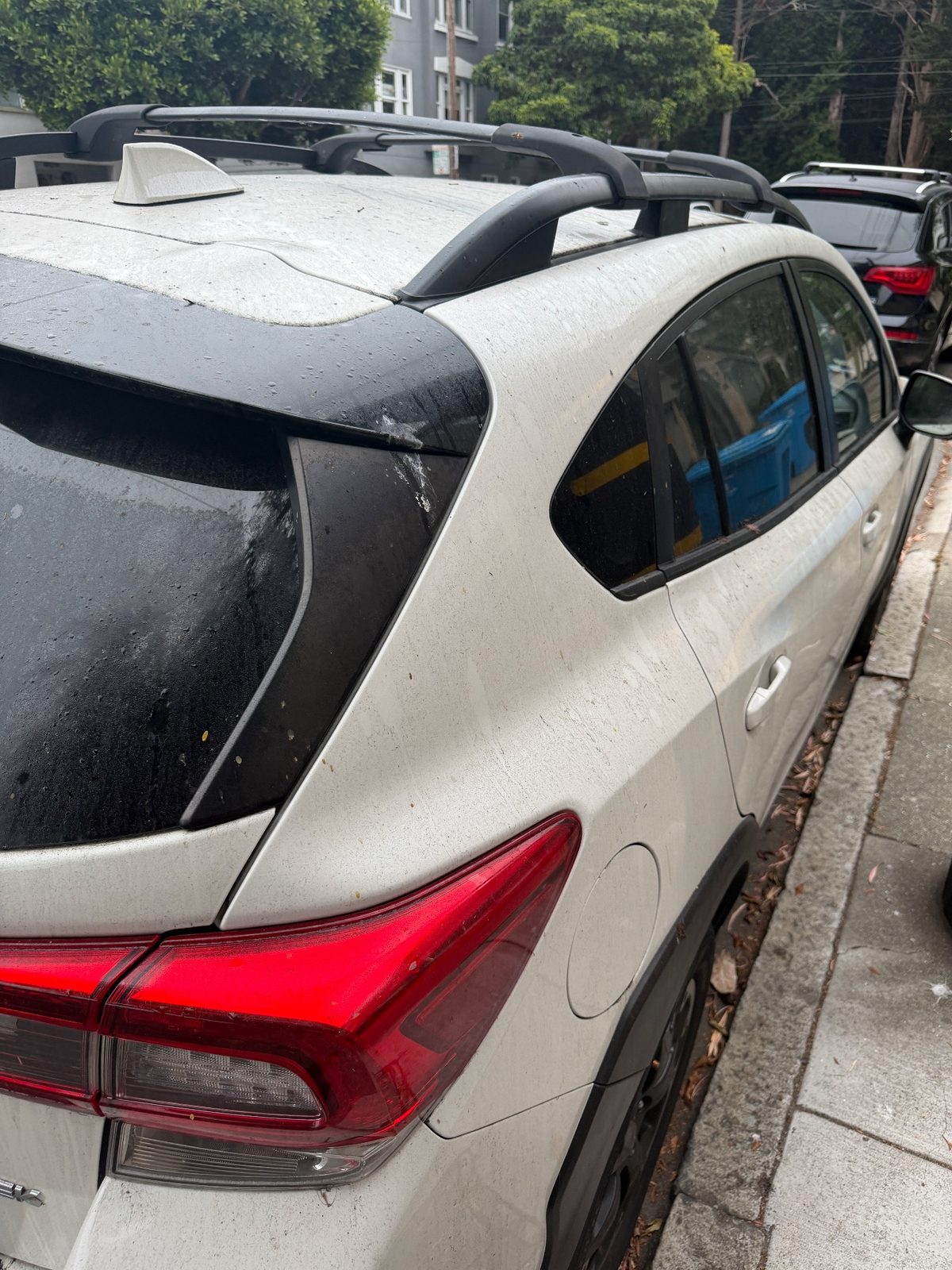 Dusty curb-side rear quarter of a white Subaru Crosstrek before washing
