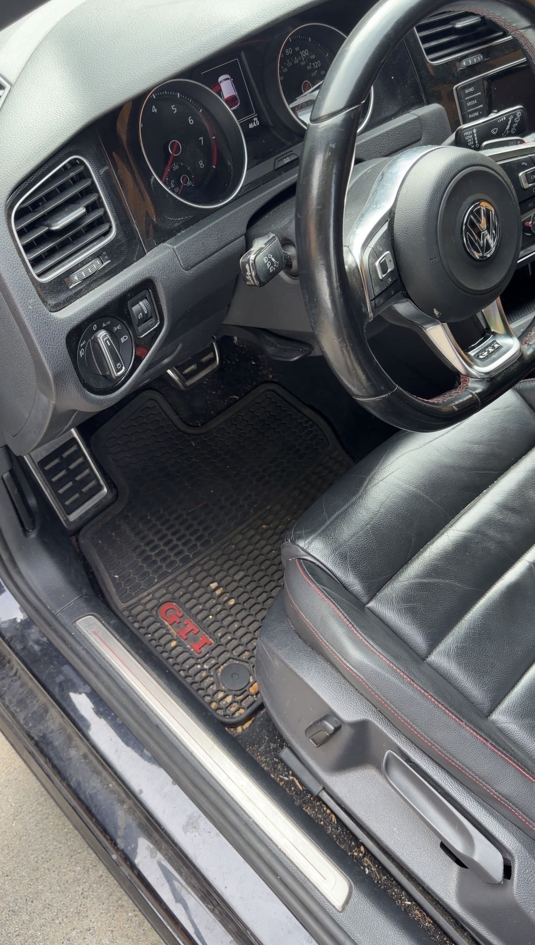 Driver footwell of a black VW GTI before cleaning, grit on the GTI rubber mat