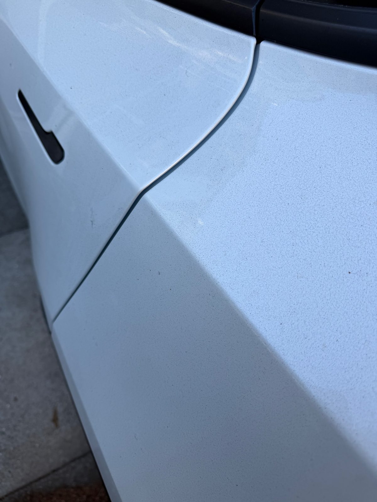 Dusty rear door and quarter panel of a white Tesla Model Y before detailing, fine grit specks across the paint