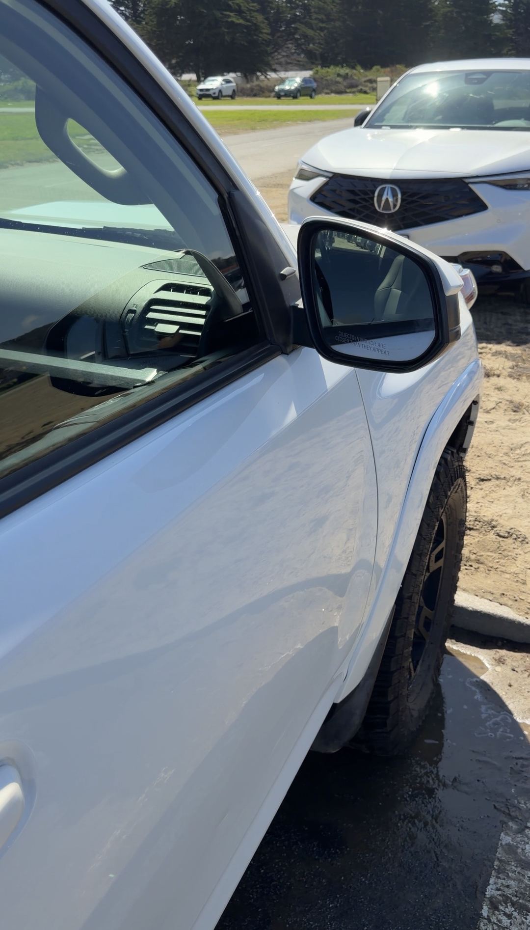 Clean front passenger door and fender of a white Toyota 4Runner beside a sandy lot