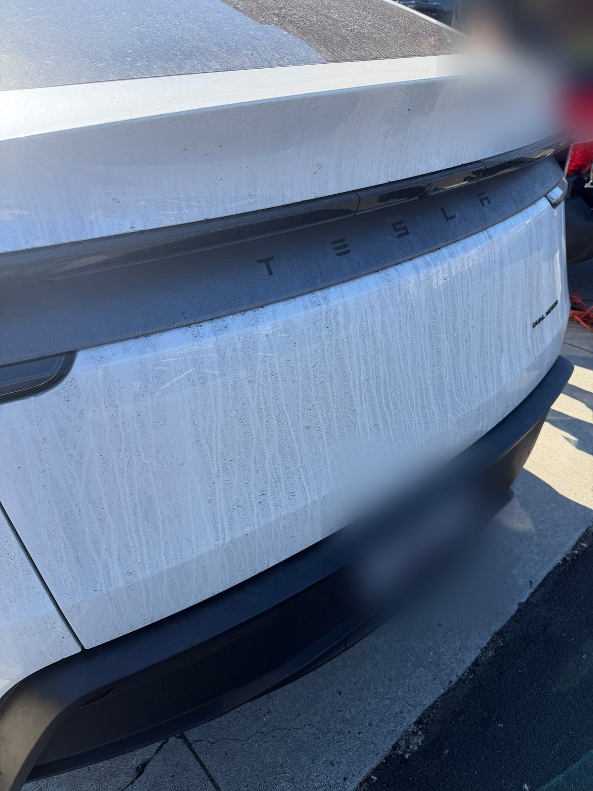 Tailgate of a white Tesla Model Y before washing, heavy white drips and dust streaks