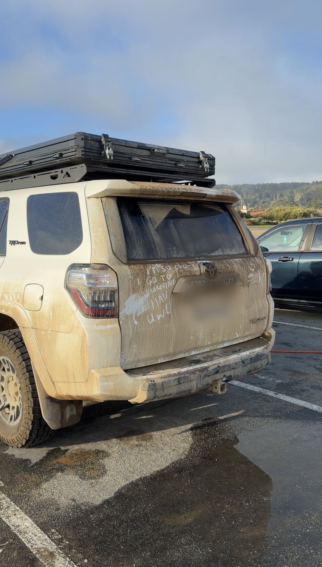 Rear of a mud-covered white Toyota 4Runner TRD Pro with a rooftop tent and writing in the dust on the tailgate