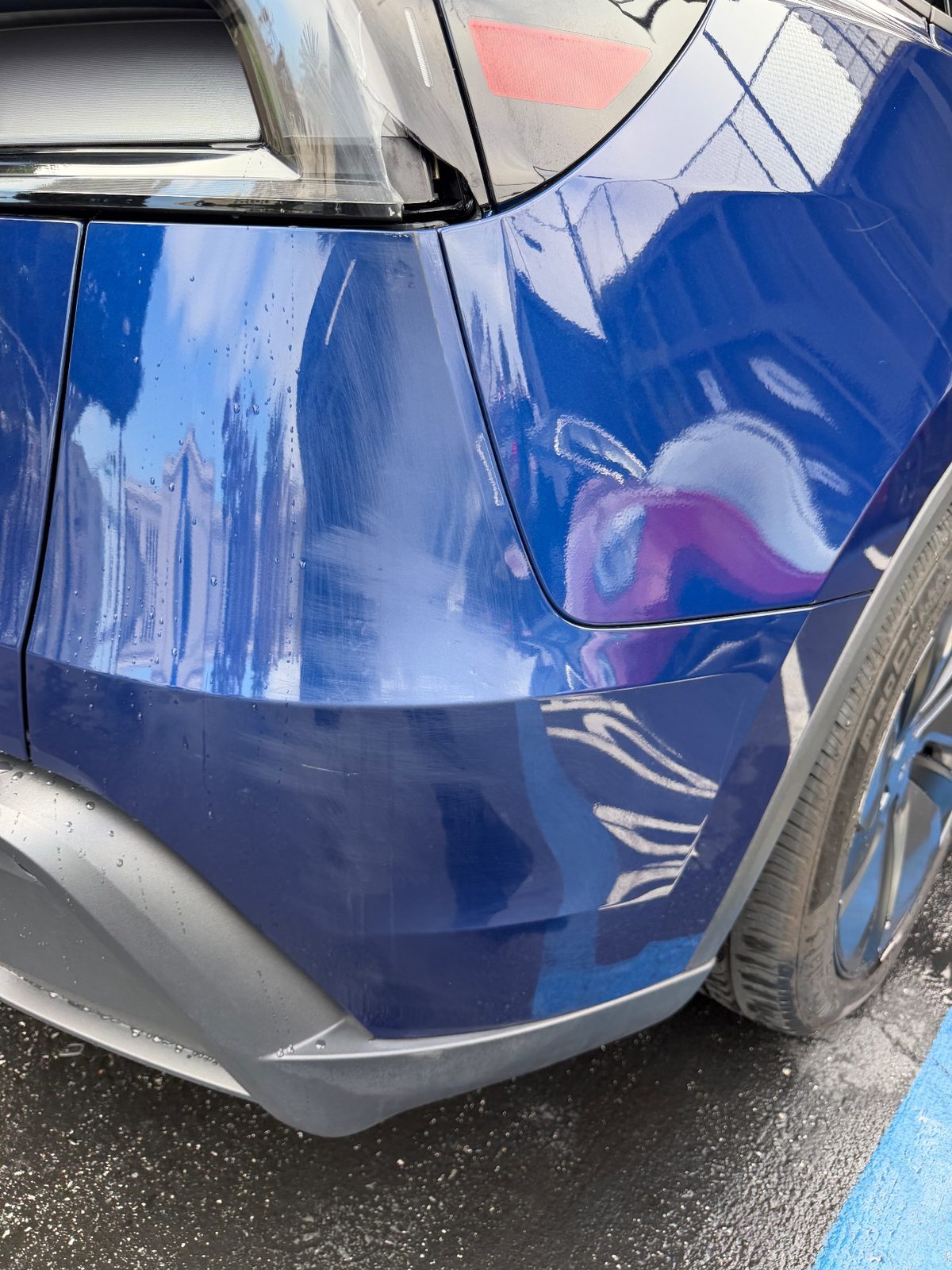 Rear bumper corner of a deep blue Tesla Model Y after detailing, white marks removed, fine scratches remaining