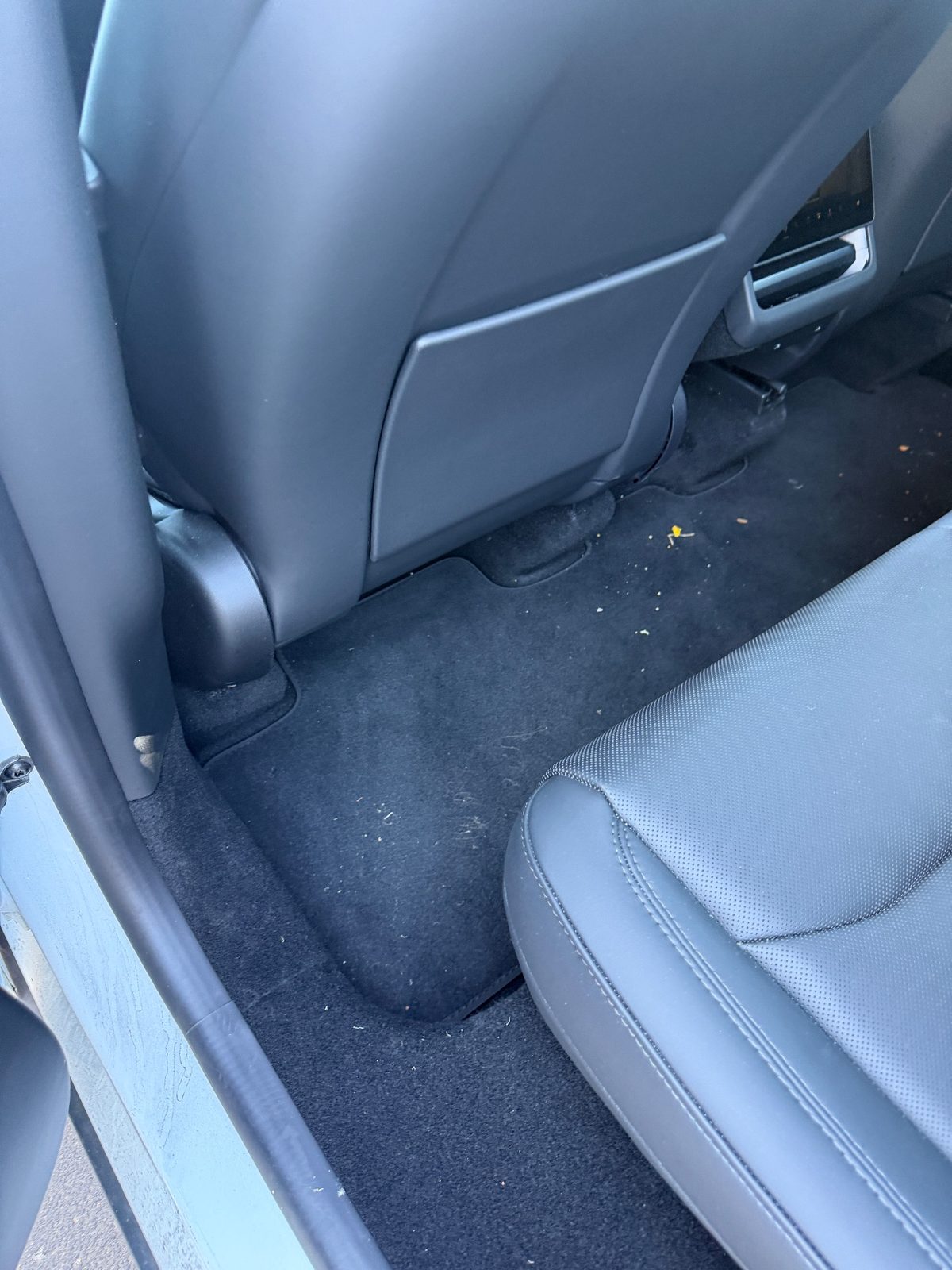 Rear footwell of a white Tesla Model Y before vacuuming, crumbs and fibres on the black mat