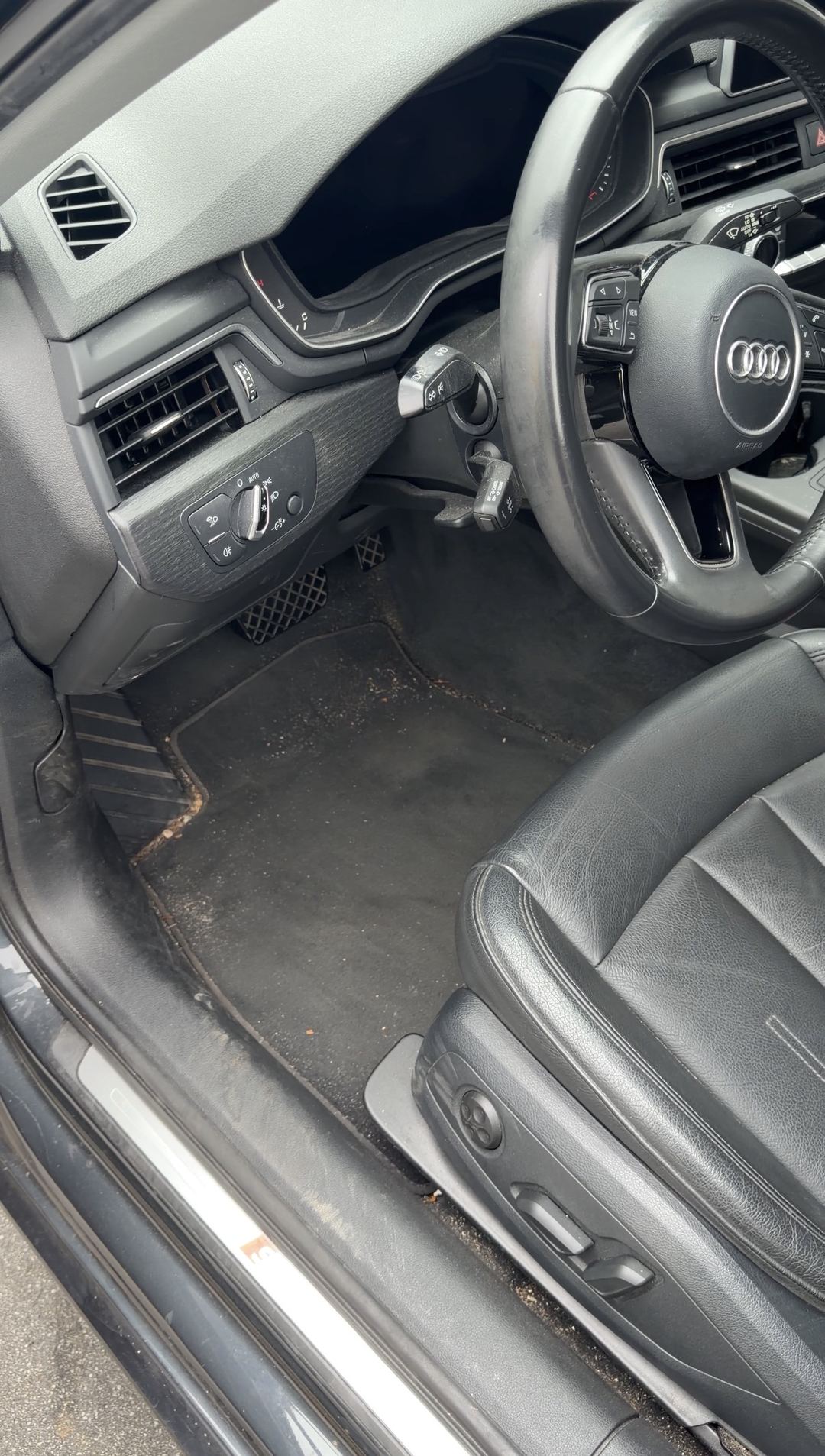 Grit and leaf debris on the driver floor mat of a grey Audi A4 with black leather seats