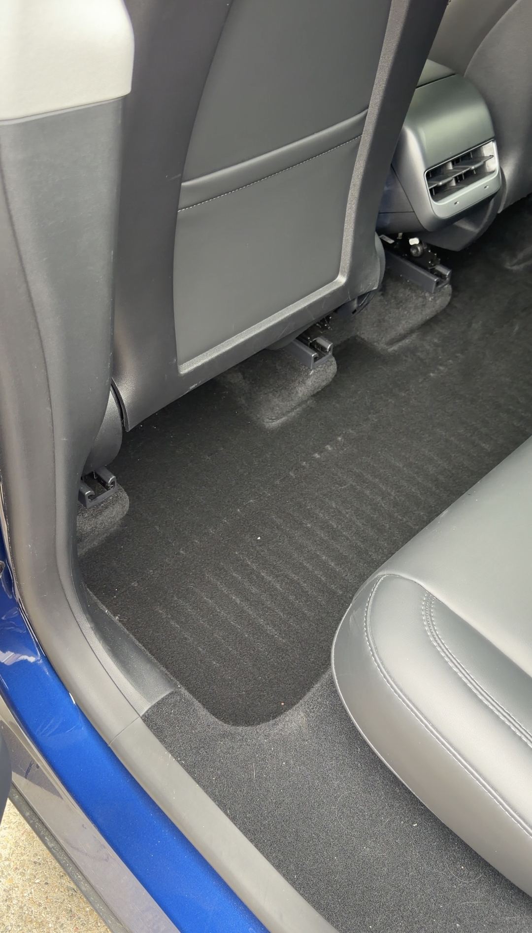 Rear driver-side footwell of a Tesla Model Y with the floor liner removed, lint visible on the carpet.