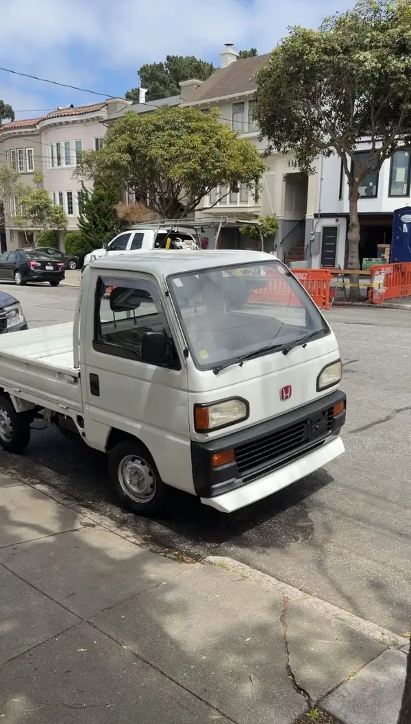 Clean white Honda Acty flat-bed kei truck parked at a kerb on a residential San Francisco street after detailing.