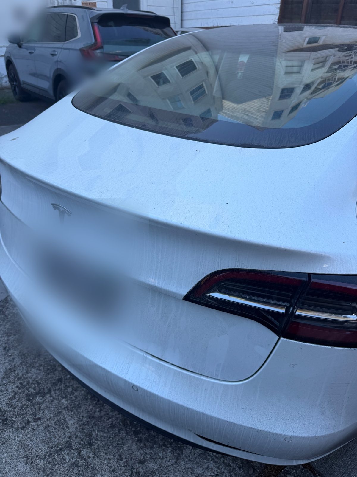 Rear of a white Tesla Model 3 before detailing, with dusty streaks on the boot lid and a hazy rear window