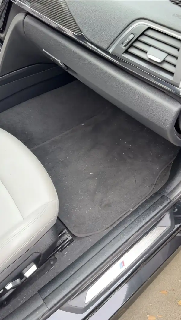 Passenger footwell of a BMW M3 before cleaning, floor mat covered in lint and loose fibres