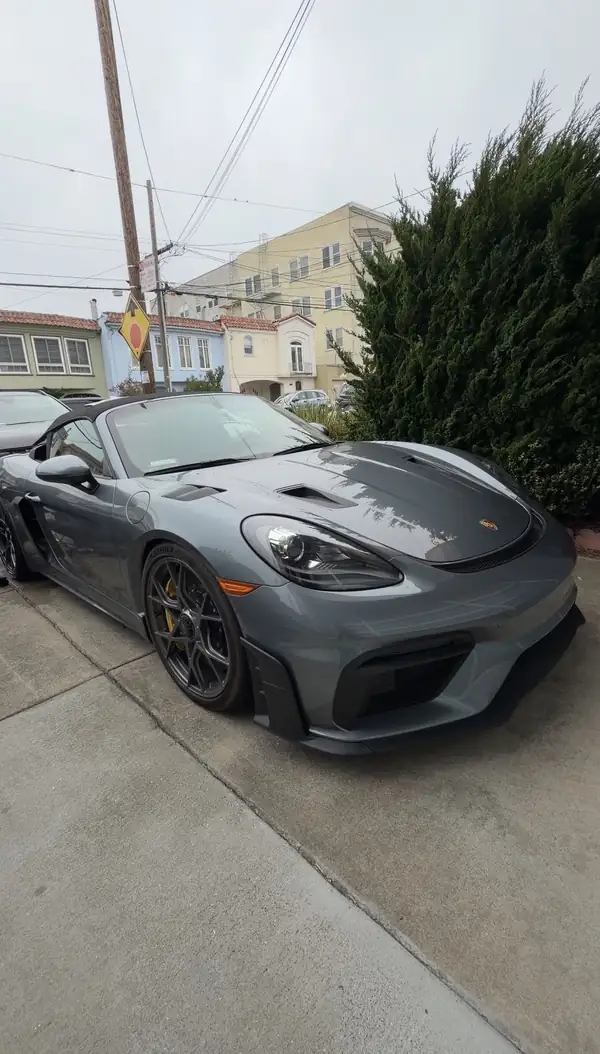 Grey Porsche 718 Spyder RS with its soft top up, parked on a San Francisco driveway before a mobile detail.