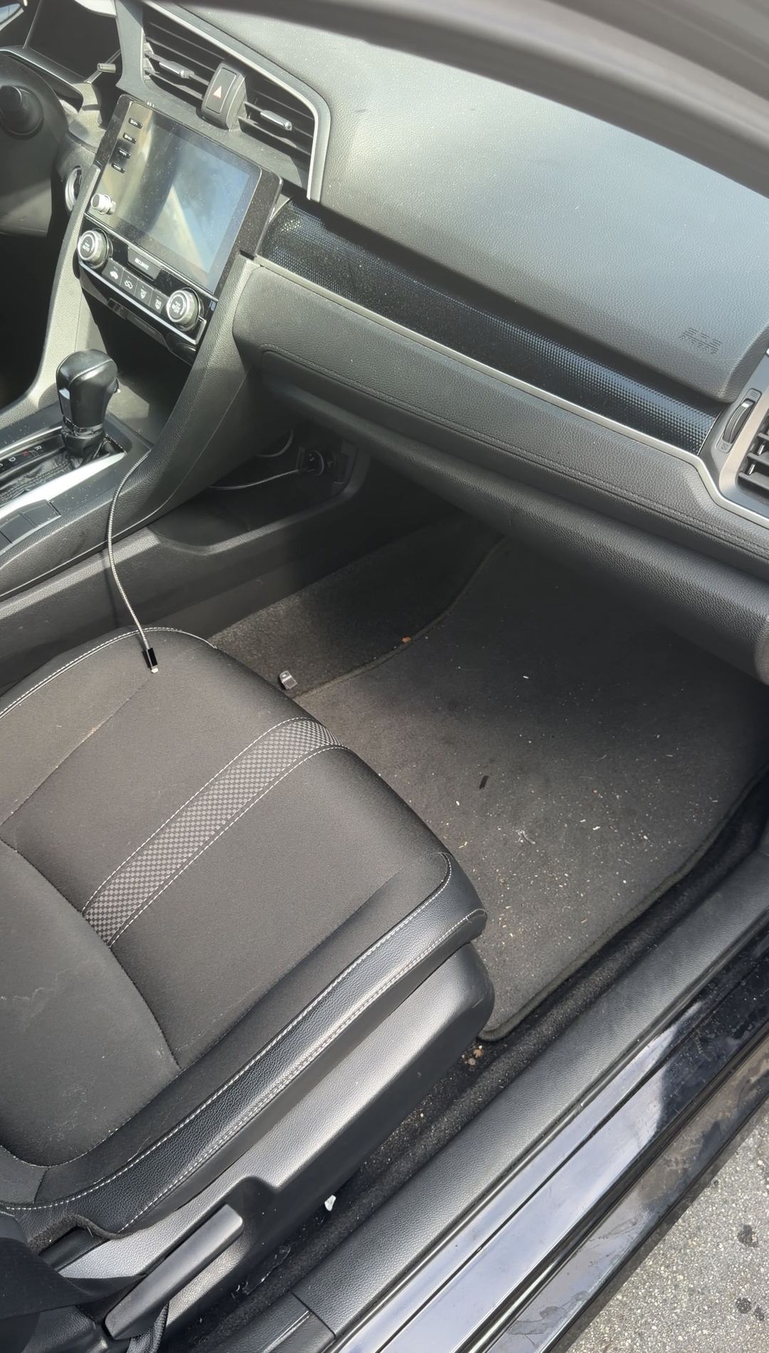 Dust and debris on the front passenger floor mat of a black Honda Civic before the detail