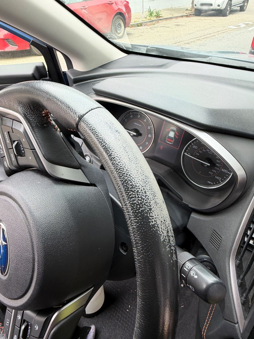 Steering wheel rim of a Subaru Crosstrek before detailing, with pale grime across the leather