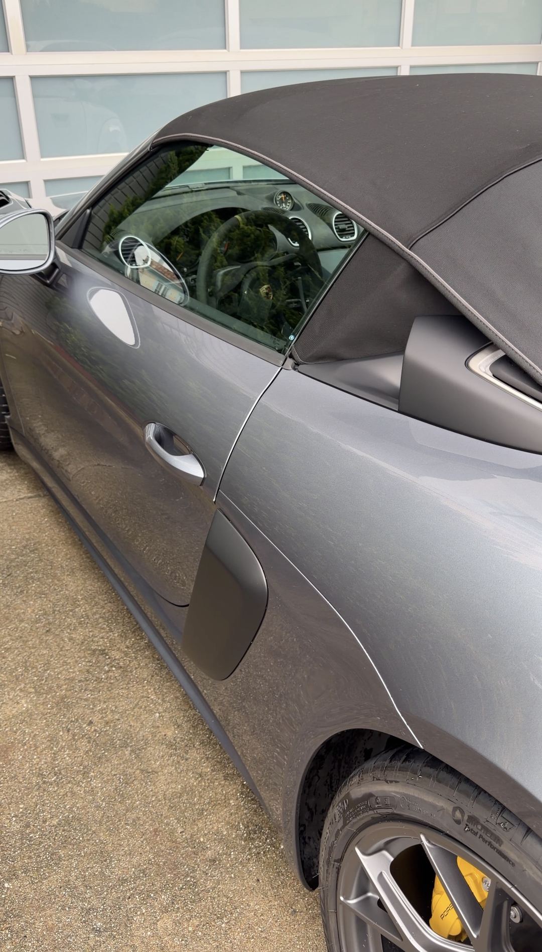 Driver's side of a grey Porsche 718 Spyder RS showing road dust on the sill before a wash.