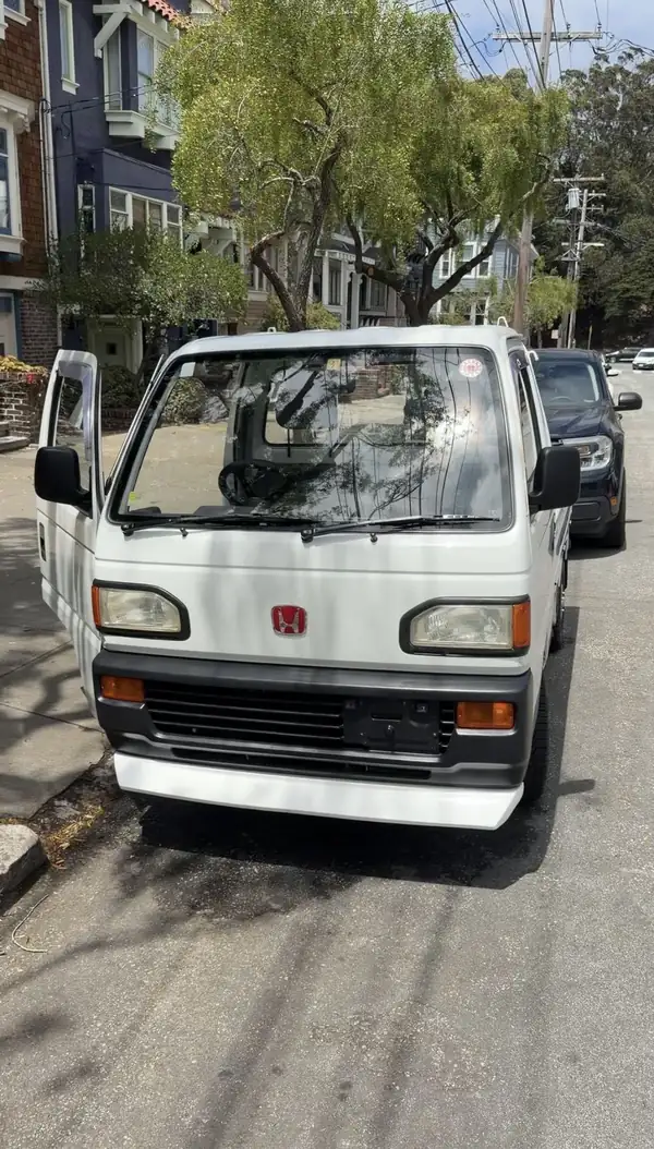 White Honda Acty kei truck seen head-on with both doors open after detailing, front panel clean and reflecting the tree canopy.