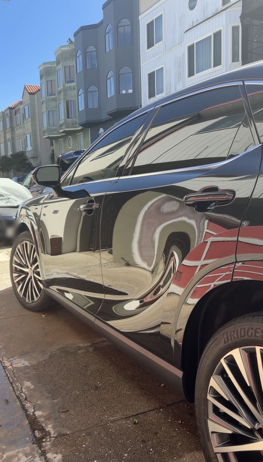 Side of a clean black Lexus RX with mirror-like reflections of a red garage door