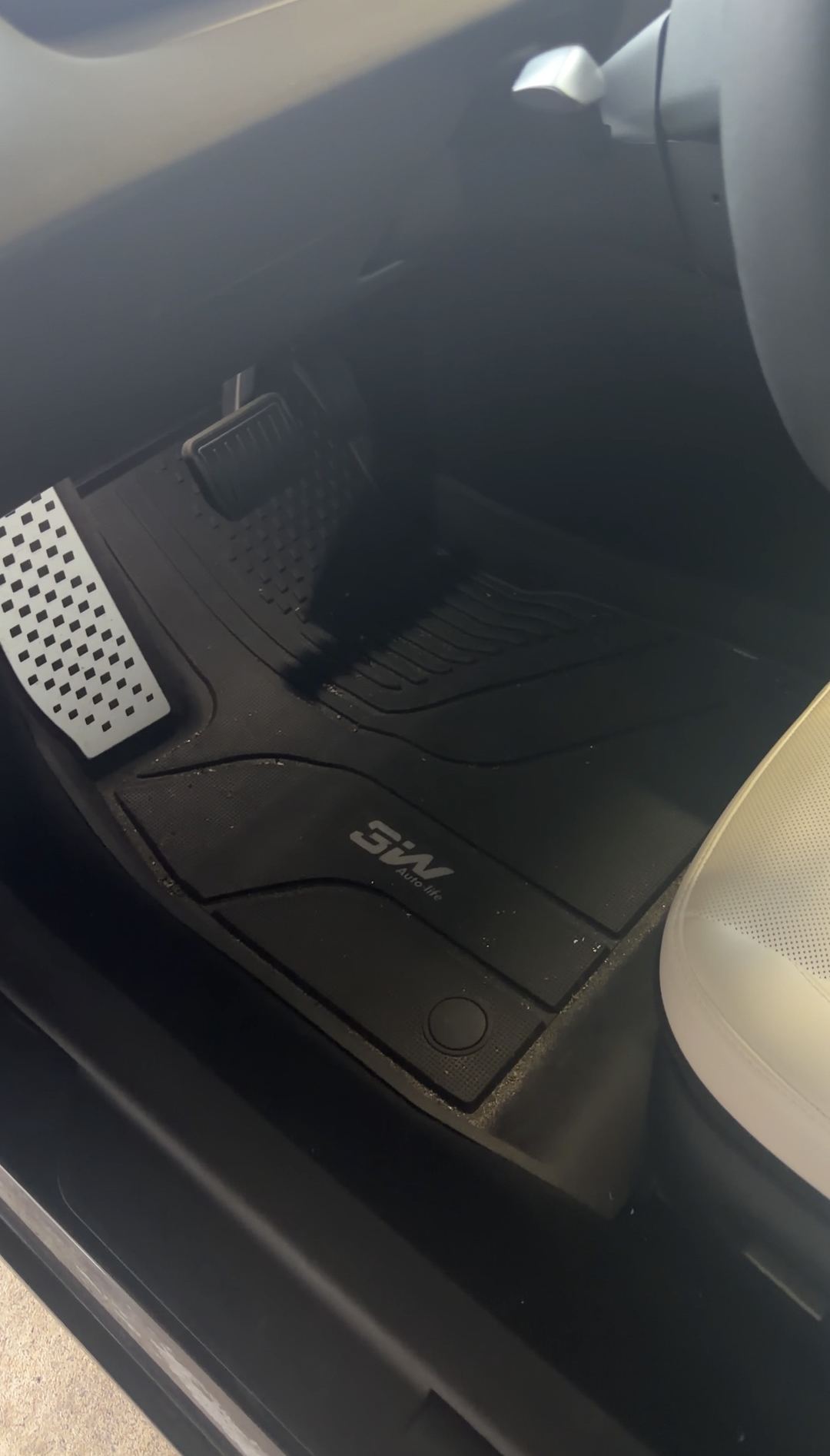 Driver's footwell of a Tesla Model 3 before detailing, with grit packed into the grooves of the black all-weather floor mat