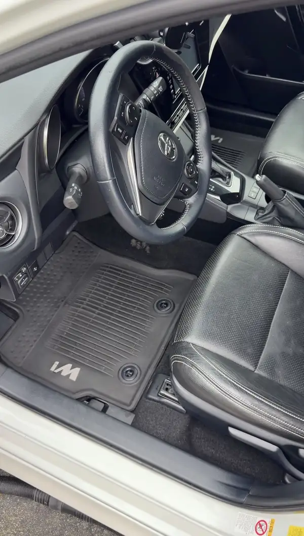 Clean driver's cockpit of a white Toyota Corolla iM after detailing, seen through the open door, with a spotless iM-branded rubber floor liner.