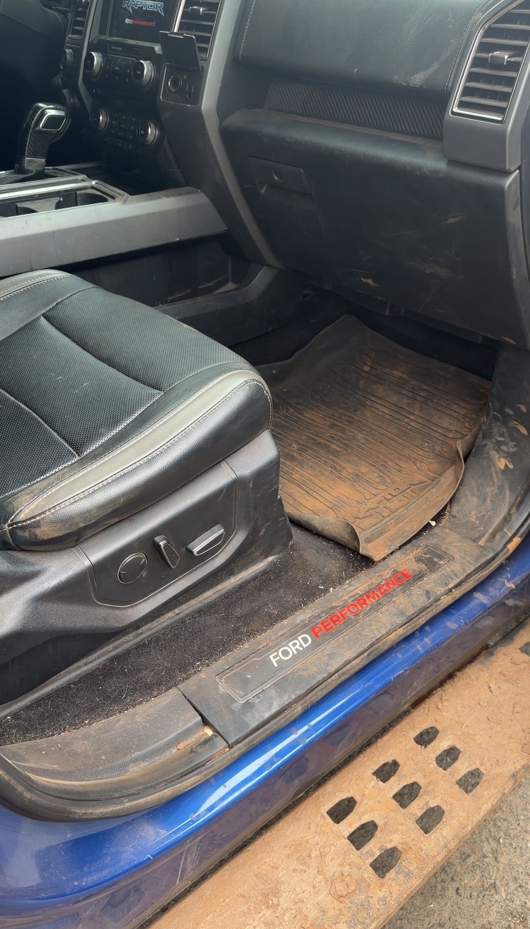 Passenger footwell of a Ford F-150 Raptor with a mud-caked floor liner before cleaning
