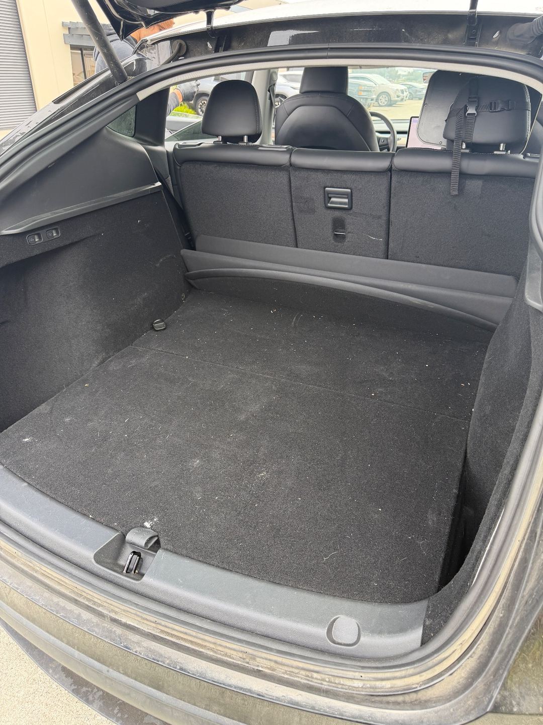 Cargo area of a black Tesla Model Y before detailing, with lint and debris on the carpet